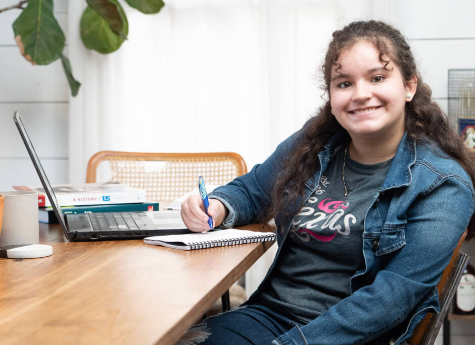 Студентка улыбается Камаре, сидящей на столе с ноутбуком.